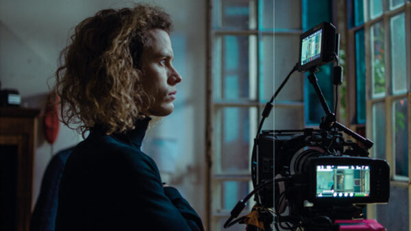 Woman with curly hair watches a professional cinema camera on a tripod by a window.