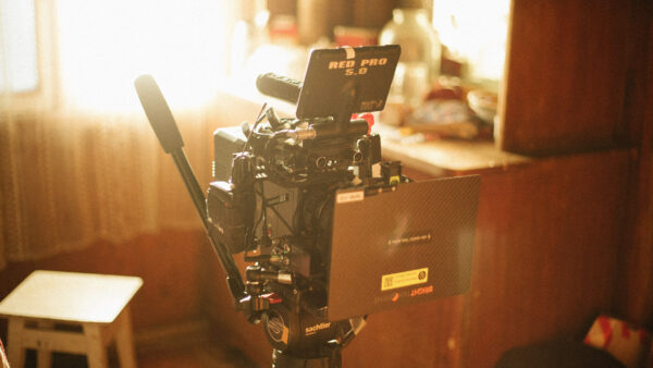 Professional cinema camera rig with external monitor on a tripod in a warmly lit room, ready for filming