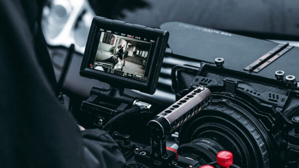 Professional video camera on a rig with an external monitor showing a scene being filmed indoors.